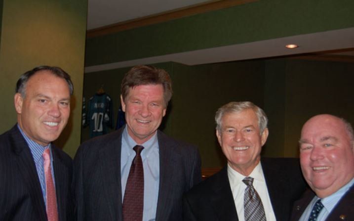 Four men in suits and ties are posing for a picture