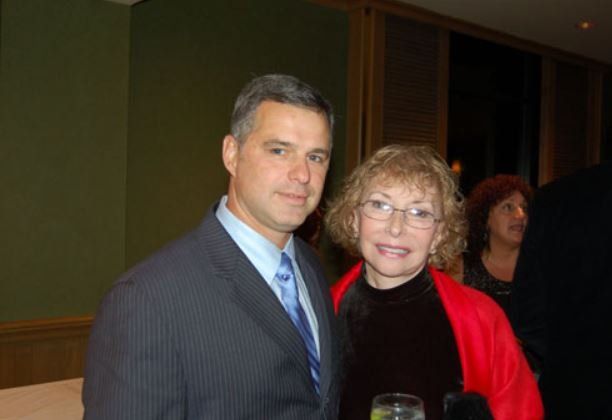 A man in a suit and tie is standing next to a woman in a red jacket.