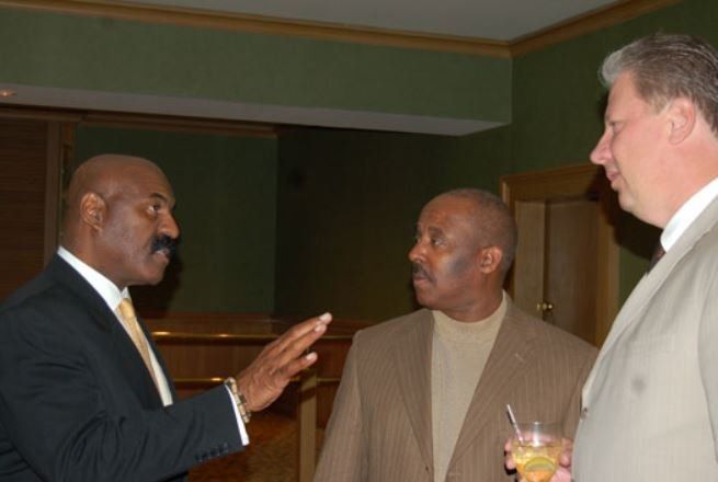 A man with a mustache is talking to two other men