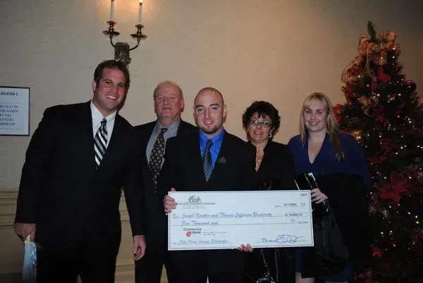 A group of people holding a large check in front of a christmas tree