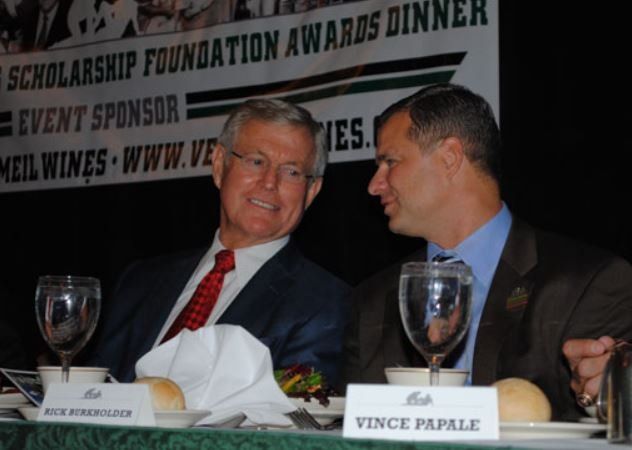 Two men sit at a table in front of a sign that says scholarship foundation awards dinner