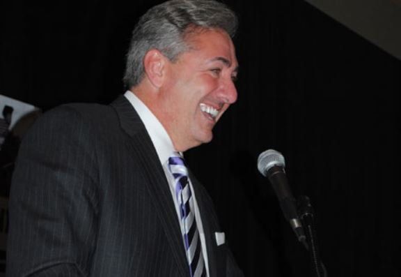 A man in a suit and tie is smiling in front of a microphone