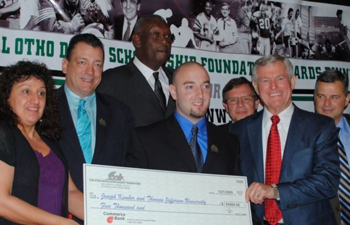 A man in a suit holds a large check in front of a group of people