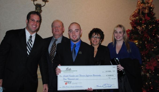 A group of people holding a large check in front of a christmas tree