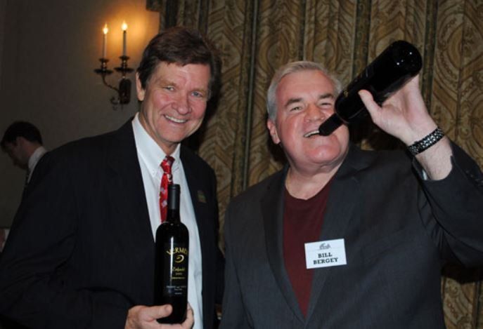 Two men standing next to each other one of whom is holding a bottle of wine