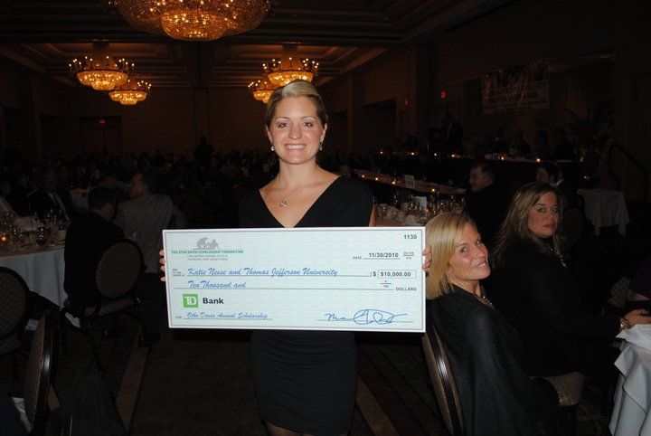 A woman is holding a large check in front of a crowd.