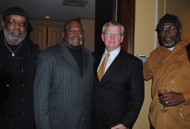 A man in a suit and tie stands between two other men
