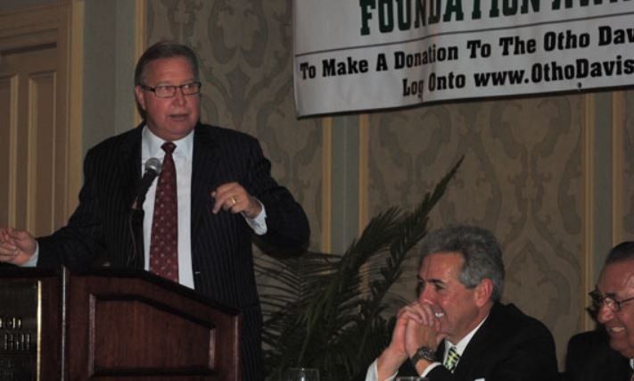 A man stands at a podium in front of a sign that says 