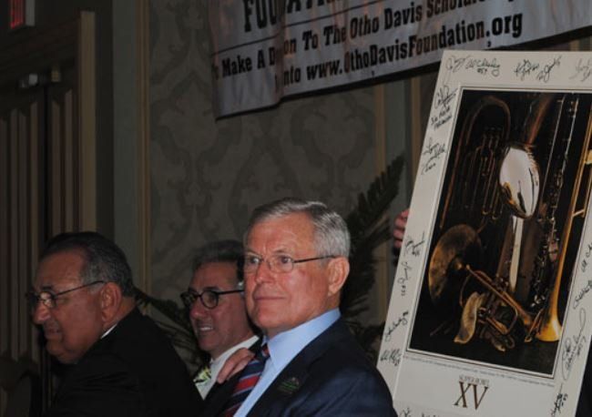 A man in a suit is holding a framed picture of a man playing a trumpet