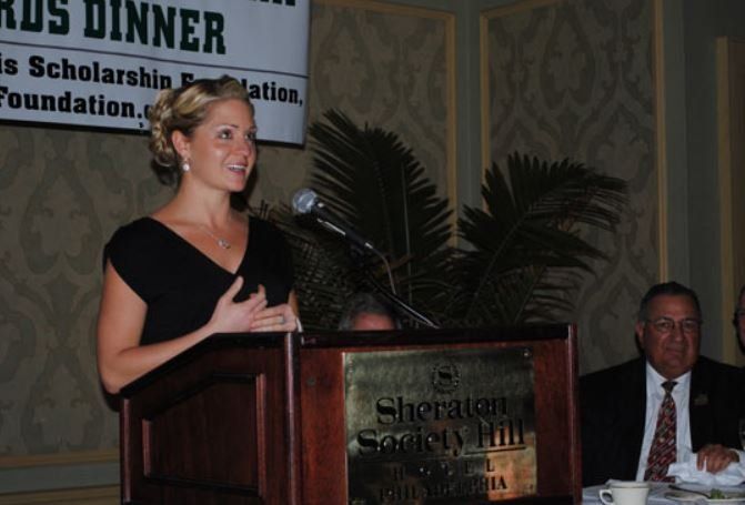 A woman stands at a podium in front of a sign that says dinner