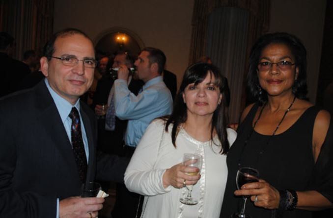 A man and two women are posing for a picture while holding wine glasses.