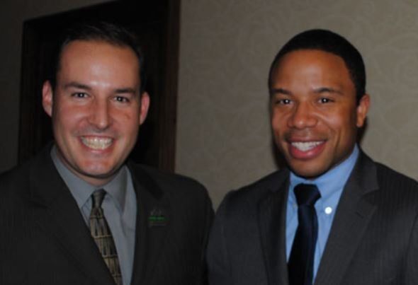Two men in suits and ties are smiling for the camera