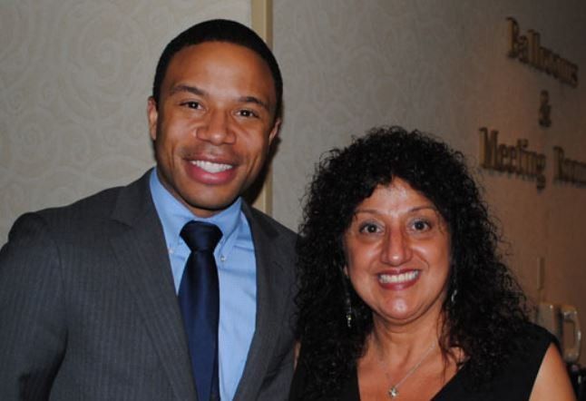 A man and a woman are posing for a picture in front of a meeting room sign