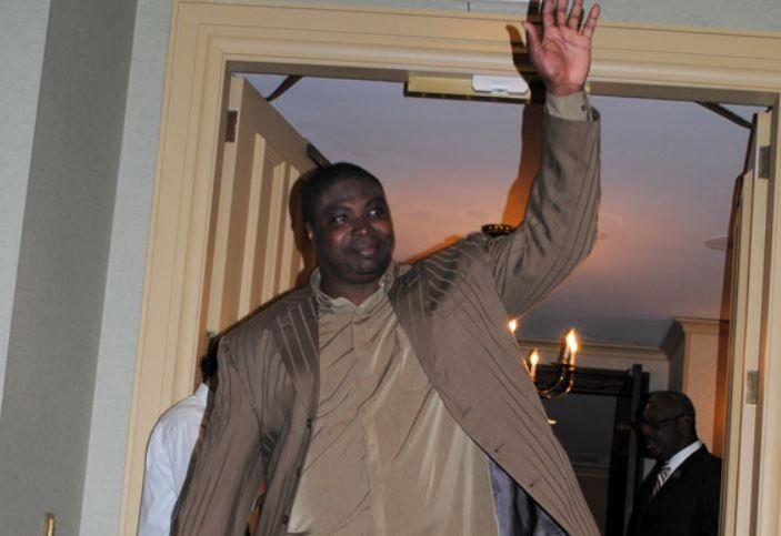 A man in a suit is waving his hand in a doorway