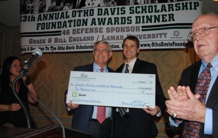 Three men are holding a check in front of a sign that says 13th annual otho davis scholarship foundation awards dinner