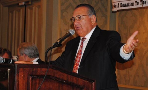 A man in a suit and tie is speaking into a microphone