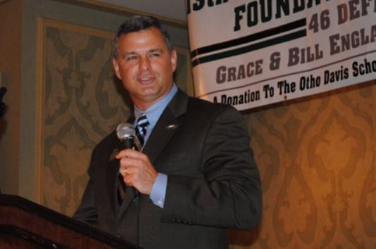 A man in a suit stands at a podium holding a microphone