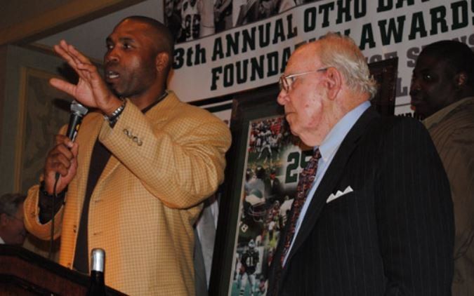 Two men standing in front of a sign that says 3th annual oth award