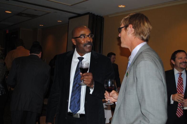 A man in a suit and tie is holding a glass of wine and talking to another man