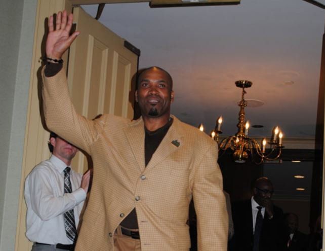 A man in a tan suit is waving his hand