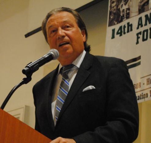 A man in a suit and tie is speaking into a microphone in front of a 14th annual foundation sign
