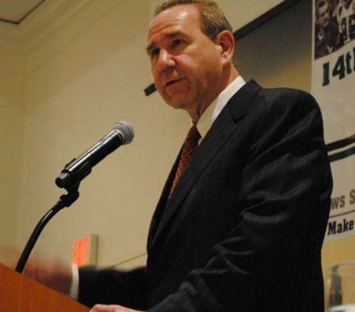 A man in a suit and tie is speaking into a microphone