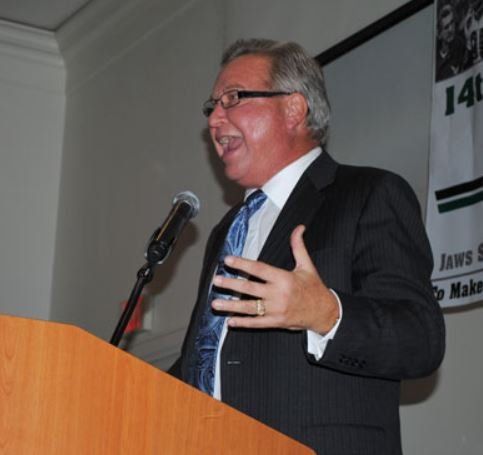 A man in a suit and tie is speaking into a microphone