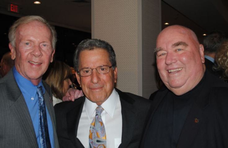 Three men are posing for a picture in front of an exit sign