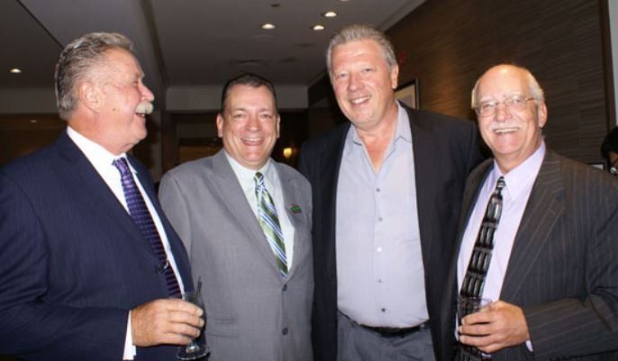 Four men in suits and ties are posing for a picture