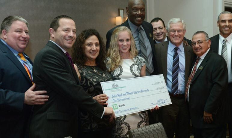 A group of people standing around a woman holding a large check
