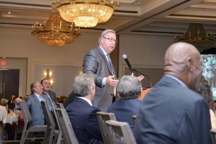 A man in a suit is giving a speech to a group of people sitting in chairs.