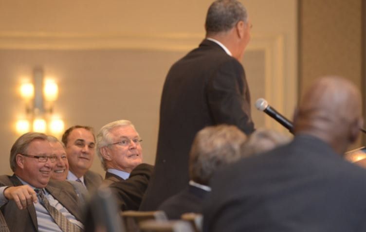 A man in a suit is giving a speech to a group of people