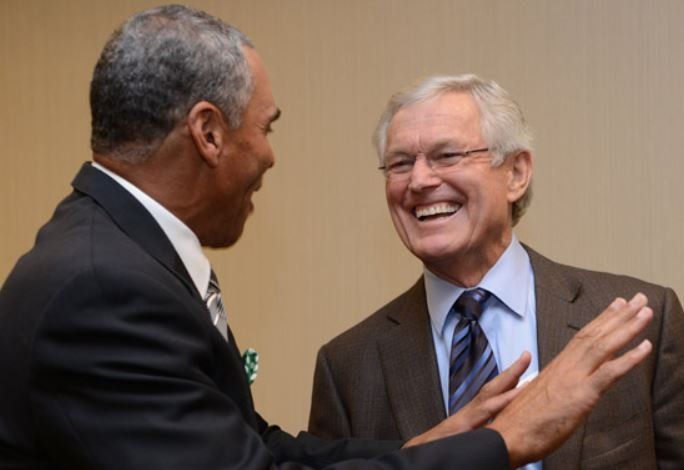 Two men in suits are laughing and shaking hands