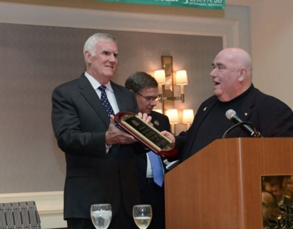 A man in a suit is giving a plaque to another man