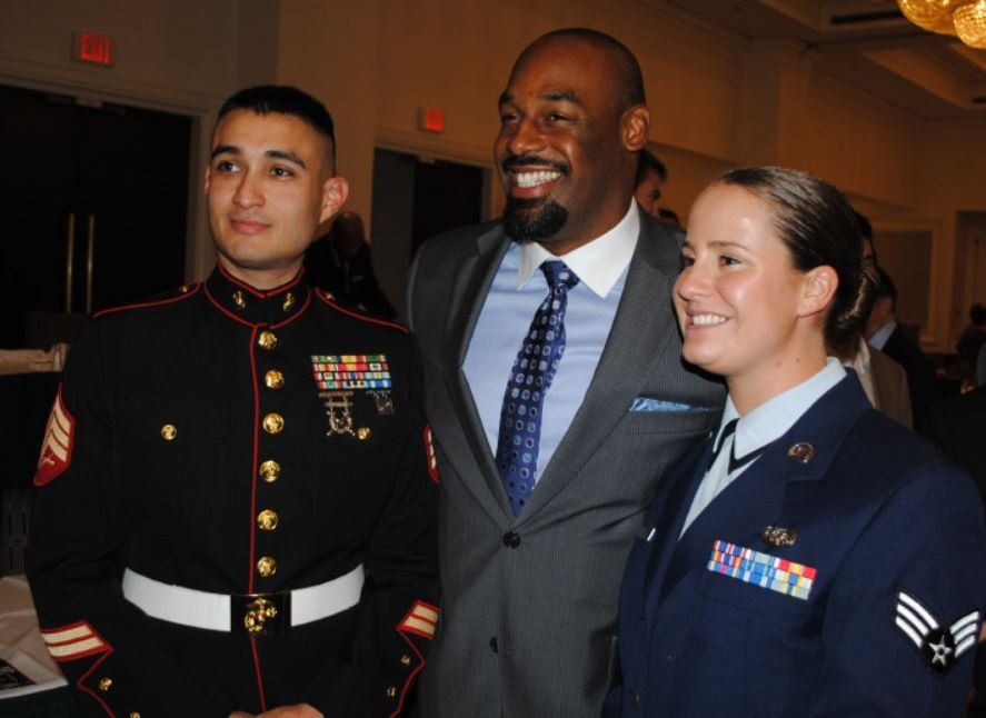 A man in a suit and tie poses for a picture with two soldiers