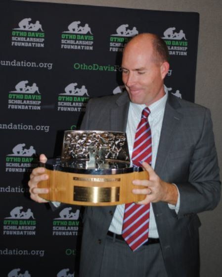 A bald man in a suit and tie is holding a trophy