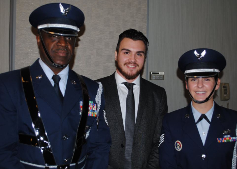 A man in a suit stands next to two men in military uniforms