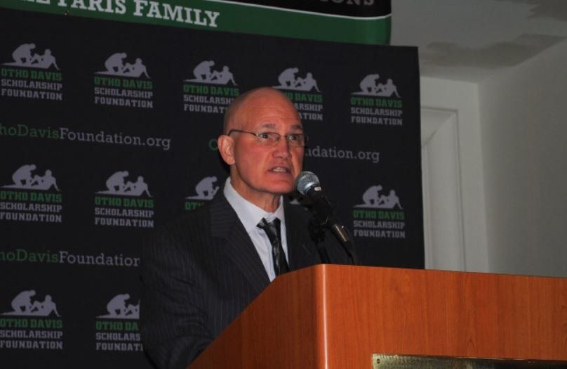 A man in a suit and tie is standing at a podium speaking into a microphone
