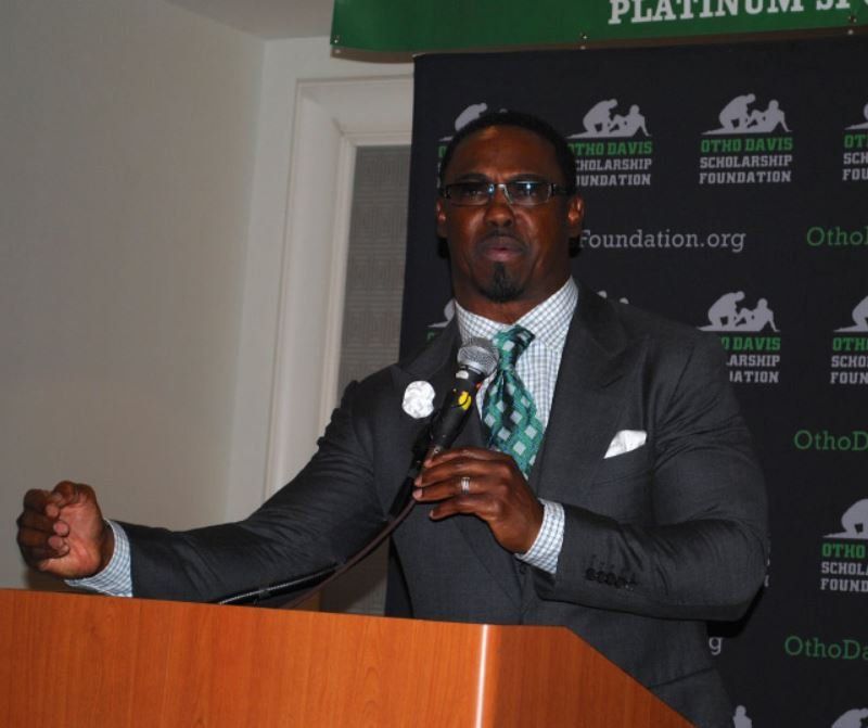 A man in a suit and tie is speaking into a microphone