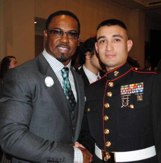 A man in a suit is shaking hands with a man in a marine uniform