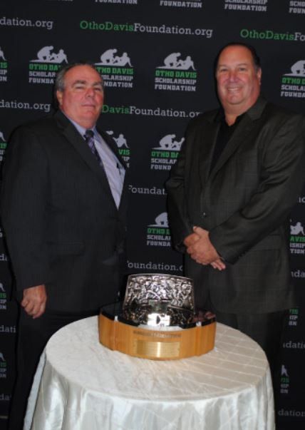Two men standing next to a table with a trophy on it