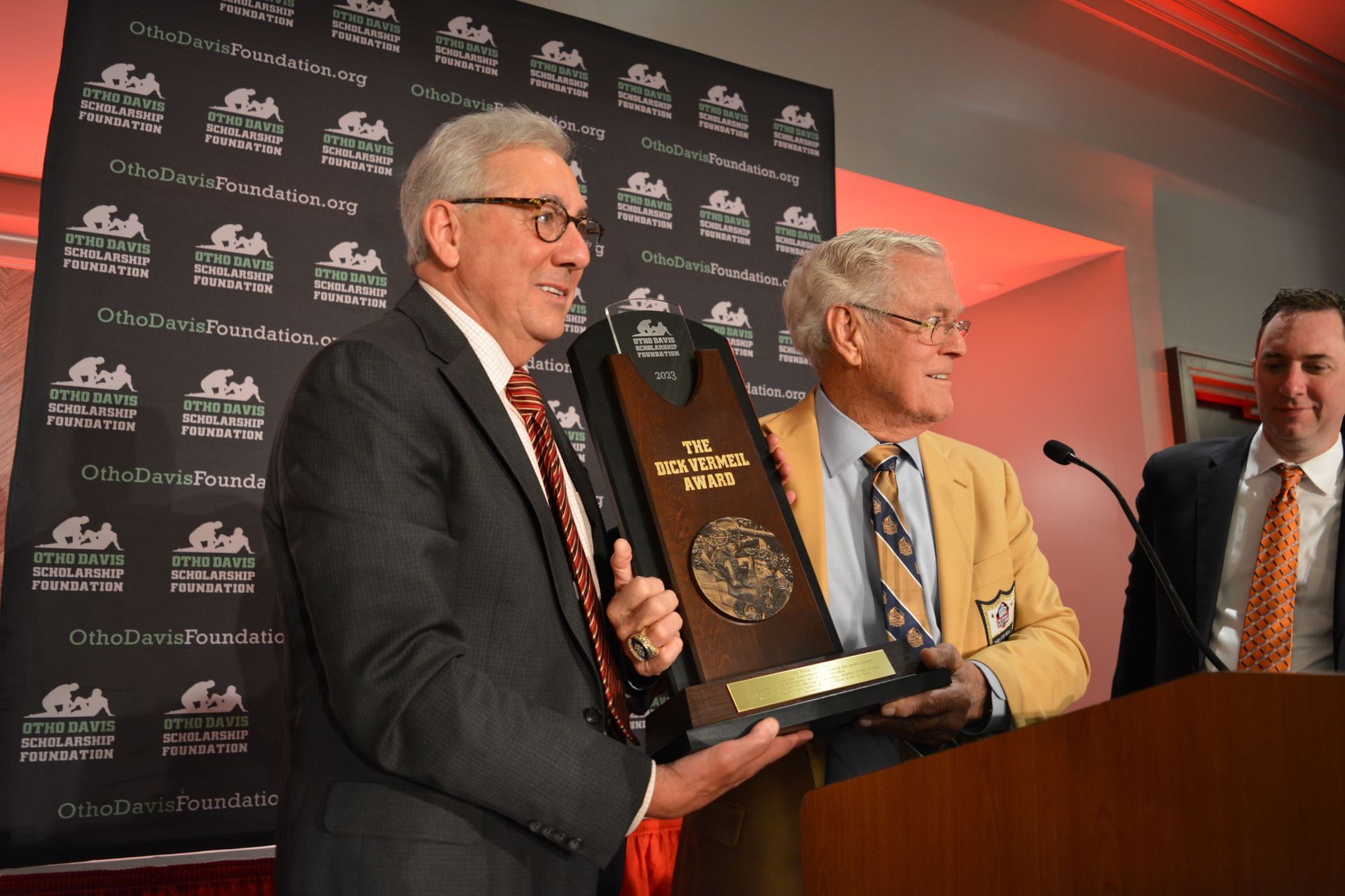 Three men in suits and ties are holding a trophy in front of a podium.