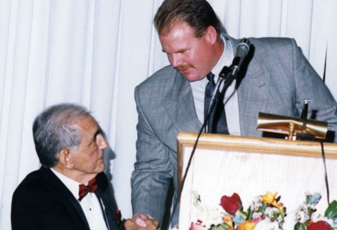 Two men shaking hands in front of a podium with flowers on it