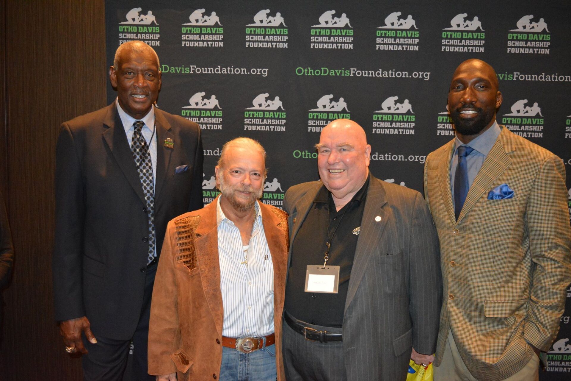 A group of men are posing for a picture in front of a wall with logos on it.