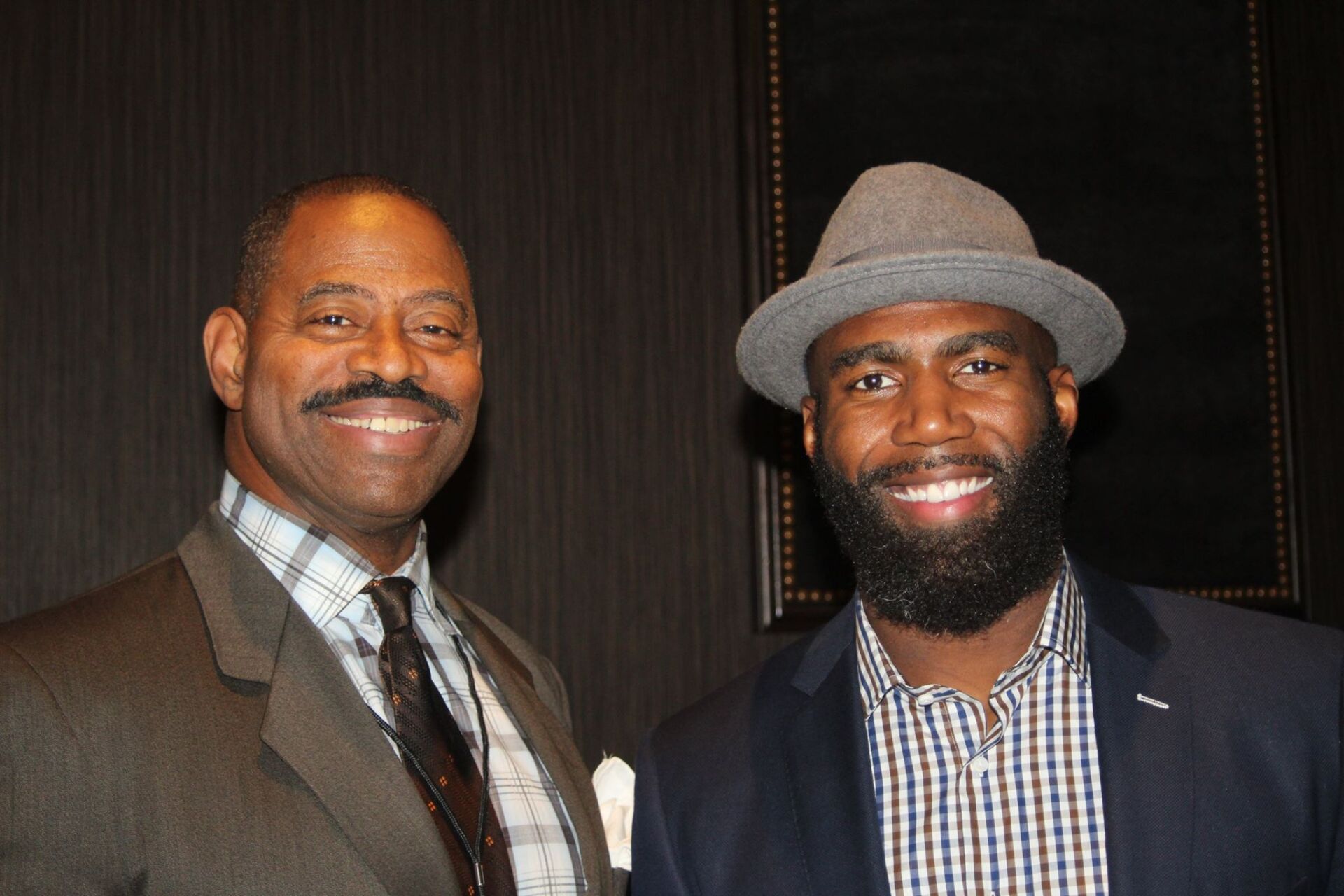Two men in suits and hats are posing for a picture.