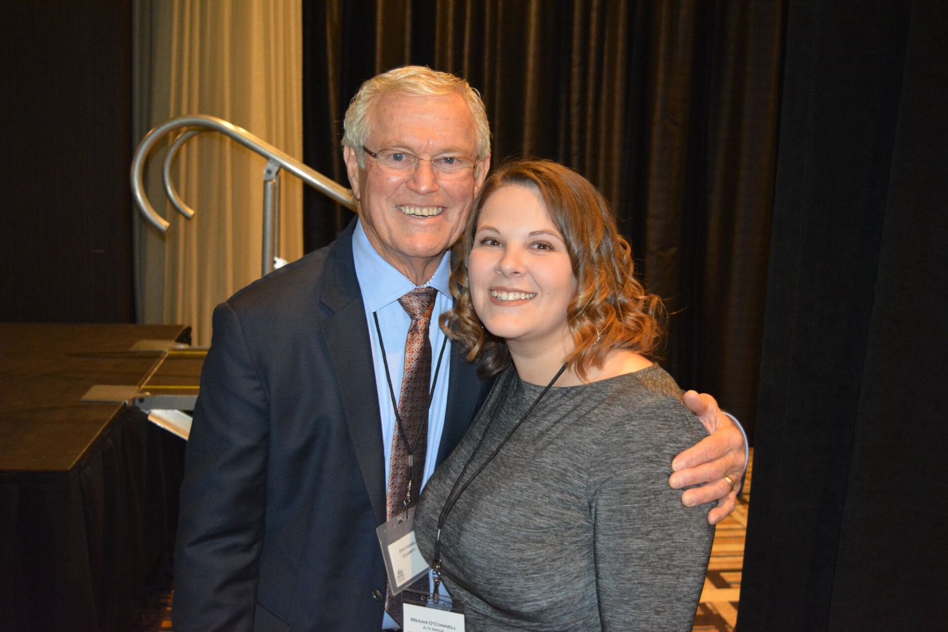 A man and a woman are posing for a picture in front of a black curtain.