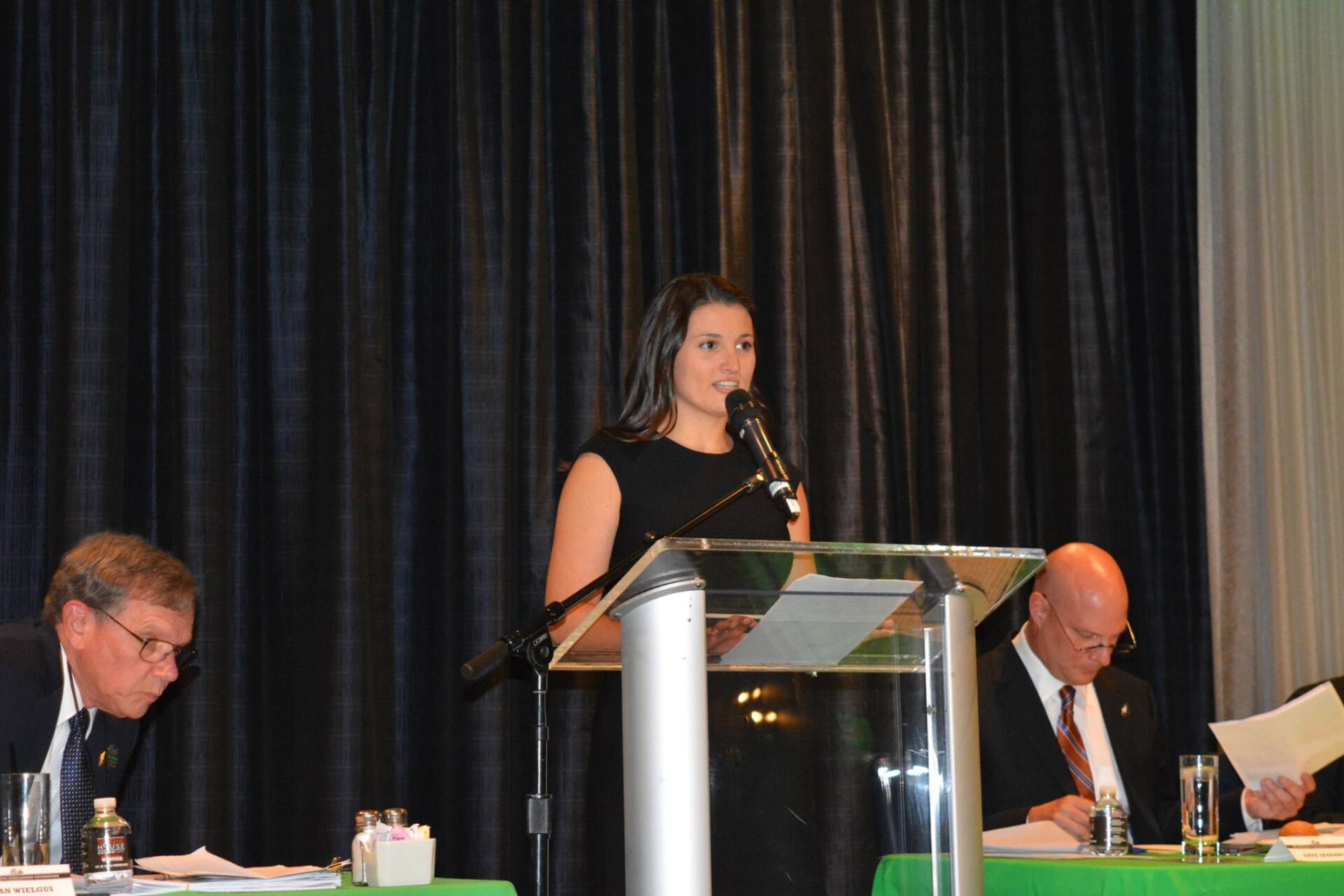 A woman is standing at a podium speaking into a microphone.