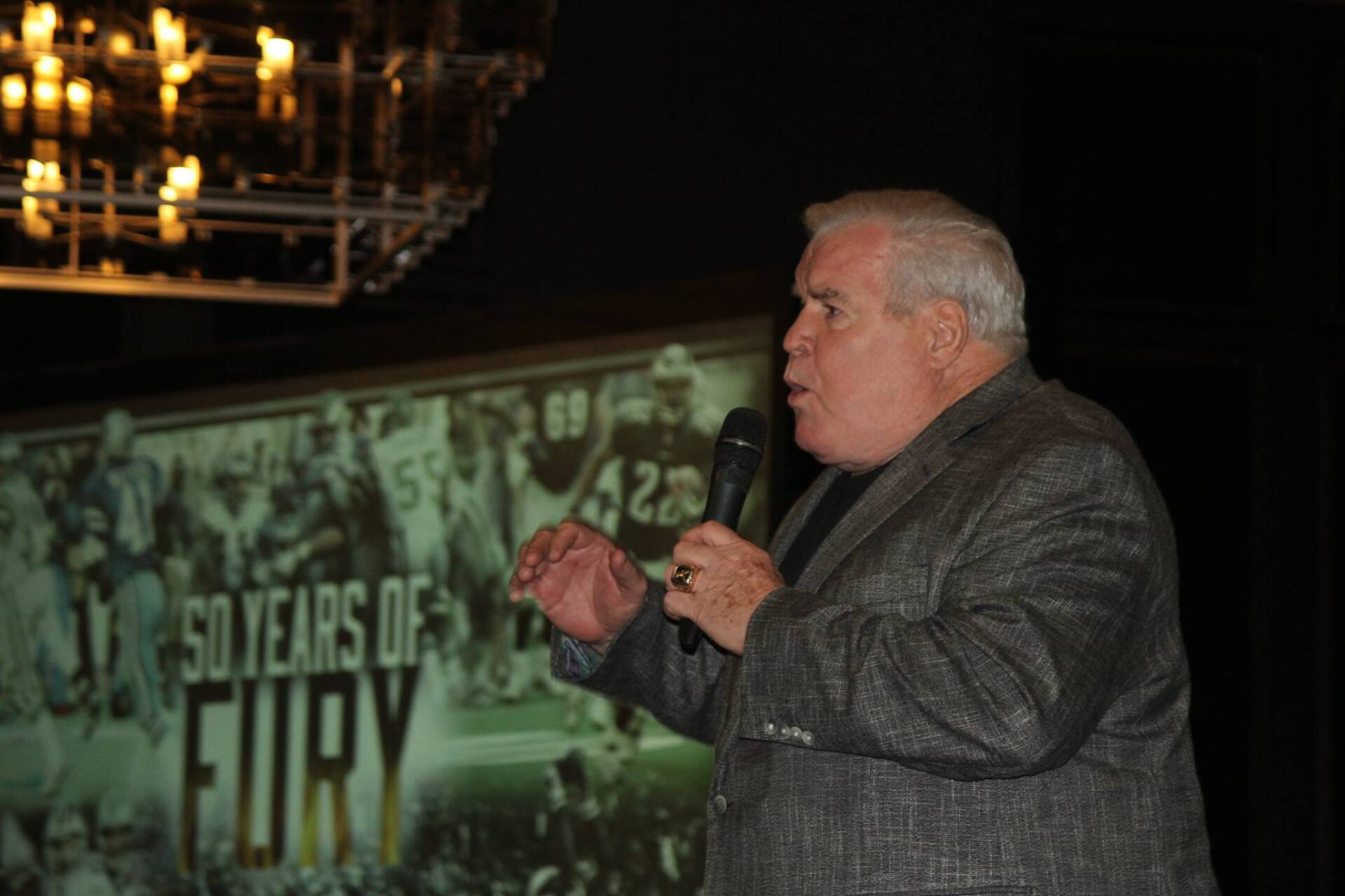 A man in a suit is holding a microphone in front of a sign that says 50 years of fury