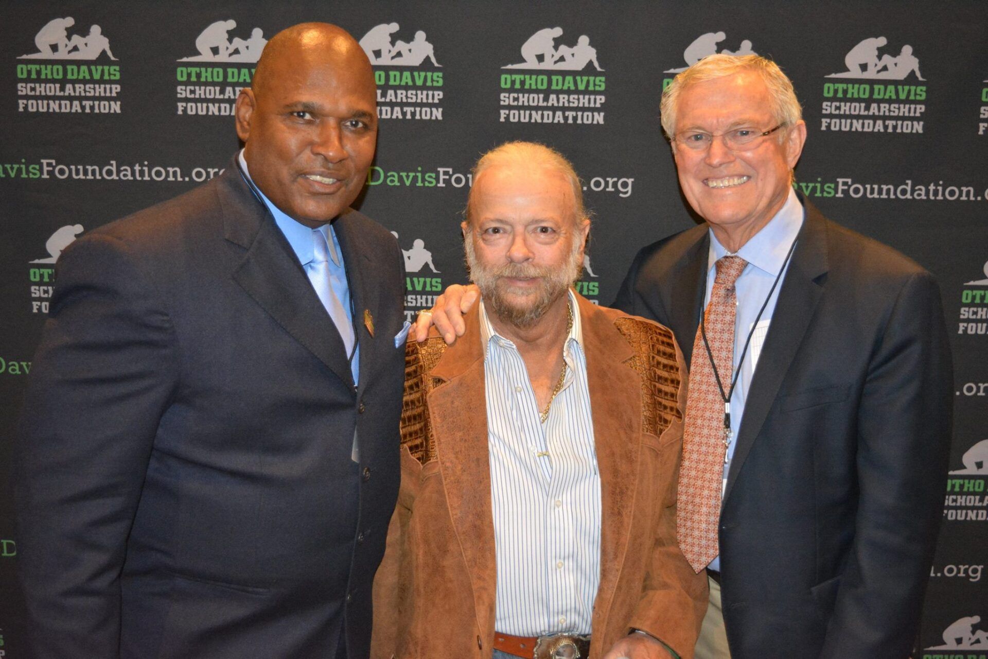 Three men are posing for a picture in front of a wall that has the word foundation on it