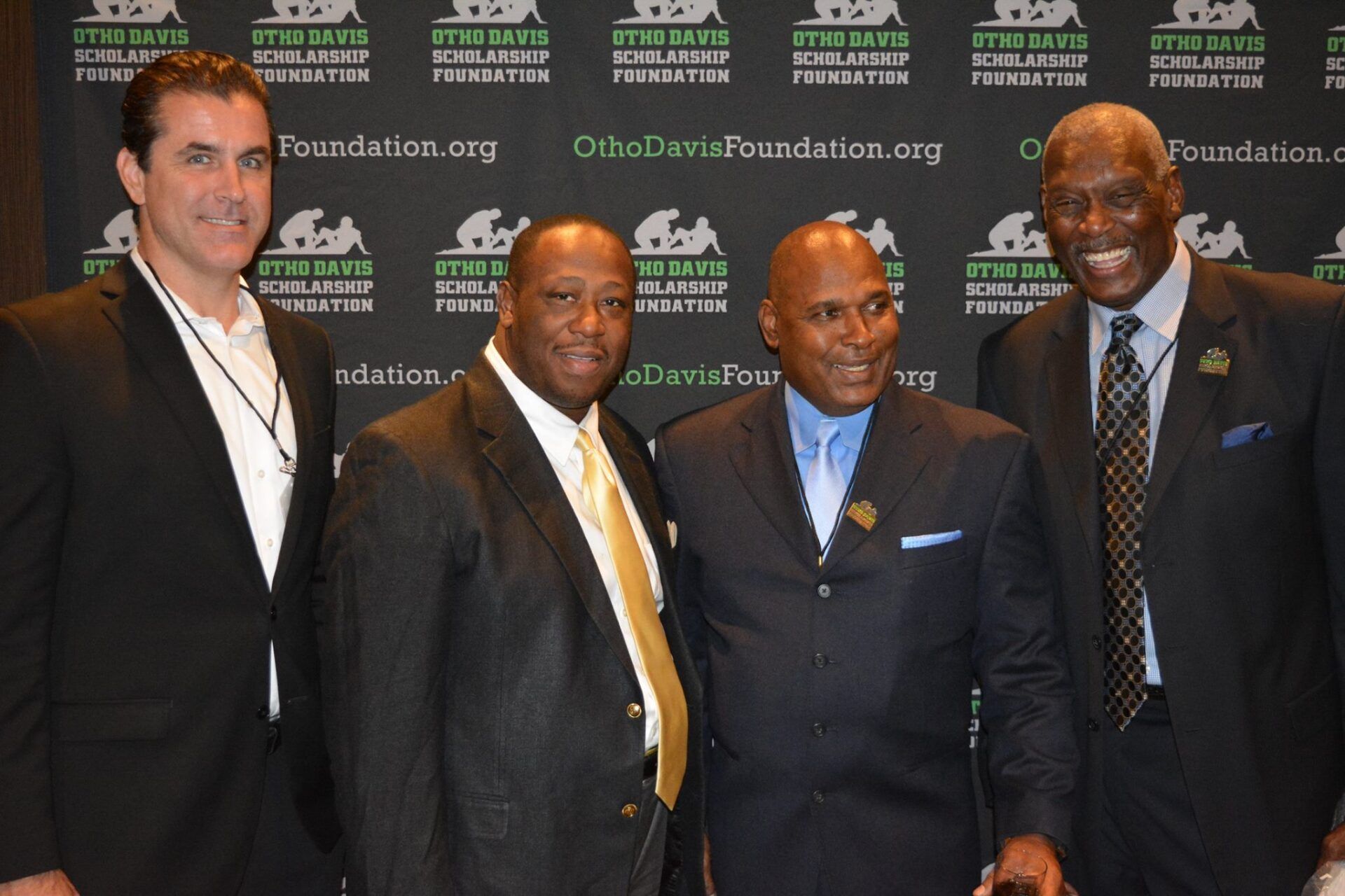 Four men are posing for a picture in front of a wall that says foundation.org